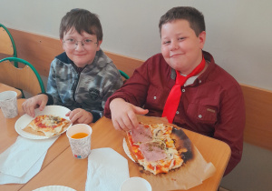 Uczniowie jedzą pizzę.