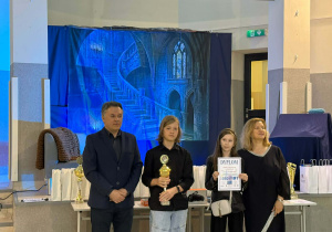 Uczniowie i nauczyciele podczas uroczystego wręczenia nagród konkursu INFOMAT. Jeden z uczniów trzyma puchar, a druga uczennica prezentuje dyplom za zajęcie III miejsca.