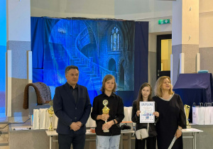 Uczniowie i nauczyciele podczas uroczystego wręczenia nagród konkursu INFOMAT. Jeden z uczniów trzyma puchar, a druga uczennica prezentuje dyplom za zajęcie III miejsca.